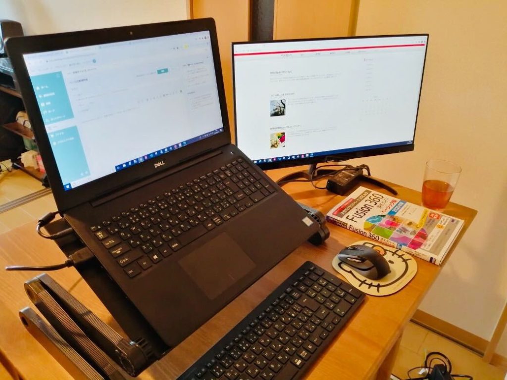 在宅勤務のデスクの様子。PCは台を用いて斜めにしている。2画面にし、作業効率をあげている。すっきりと整頓してある。